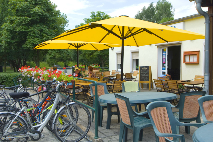Malá venkovní restaurace se stoly a židlemi, dvěma žlutými slunečníky a parkovacím místem pro kola.