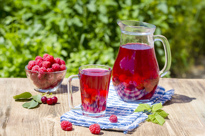 Carafe and a glass of red juice and a bowl of raspberries
