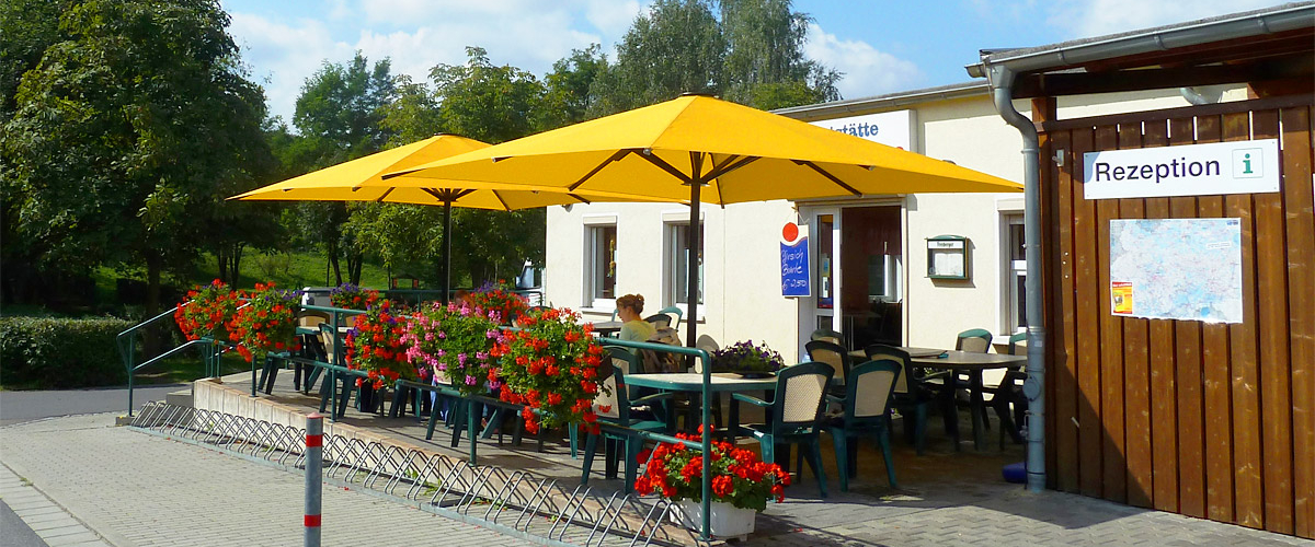 Small outdoor restaurant area with tables and chairs, two yellow parasols, and a bicycle parking area.