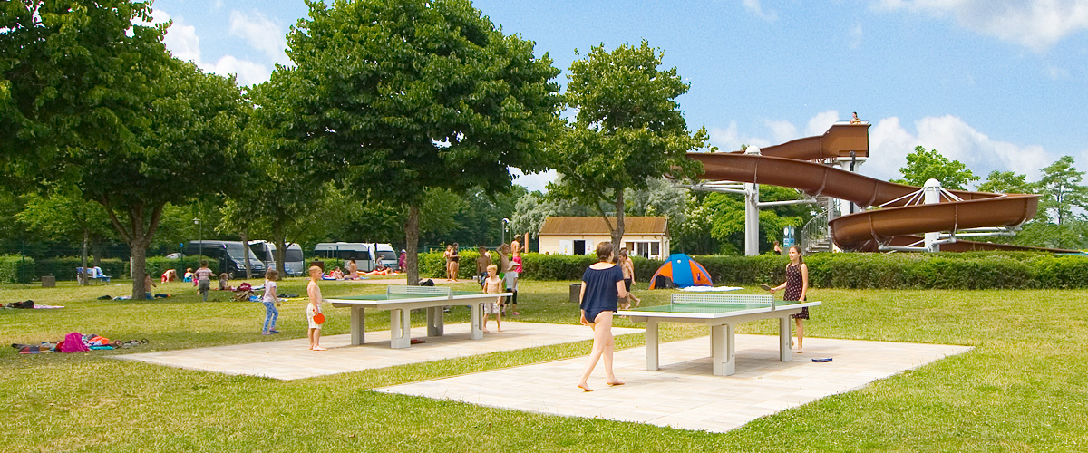 Green area with 2 table tennis tables, in the background giant slide of the adventure pool