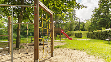 shady playground with climbing frame, seesaws and slide