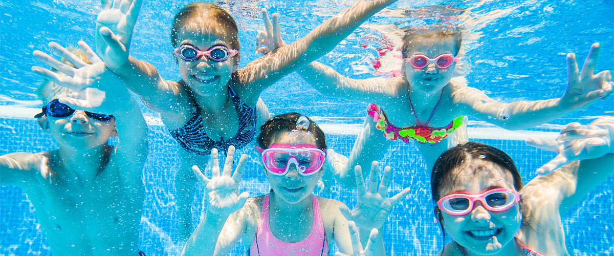 Five children with swimming goggles diving happily in the water